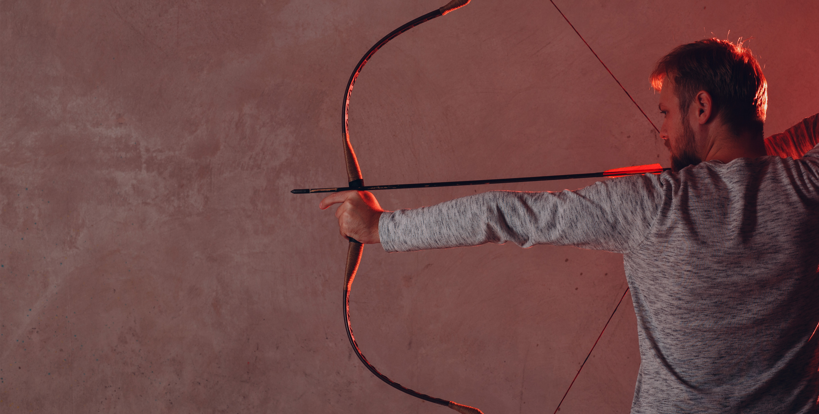 An archer holds his pose, bow aimed, arm outstretched, ready to release his arrow.