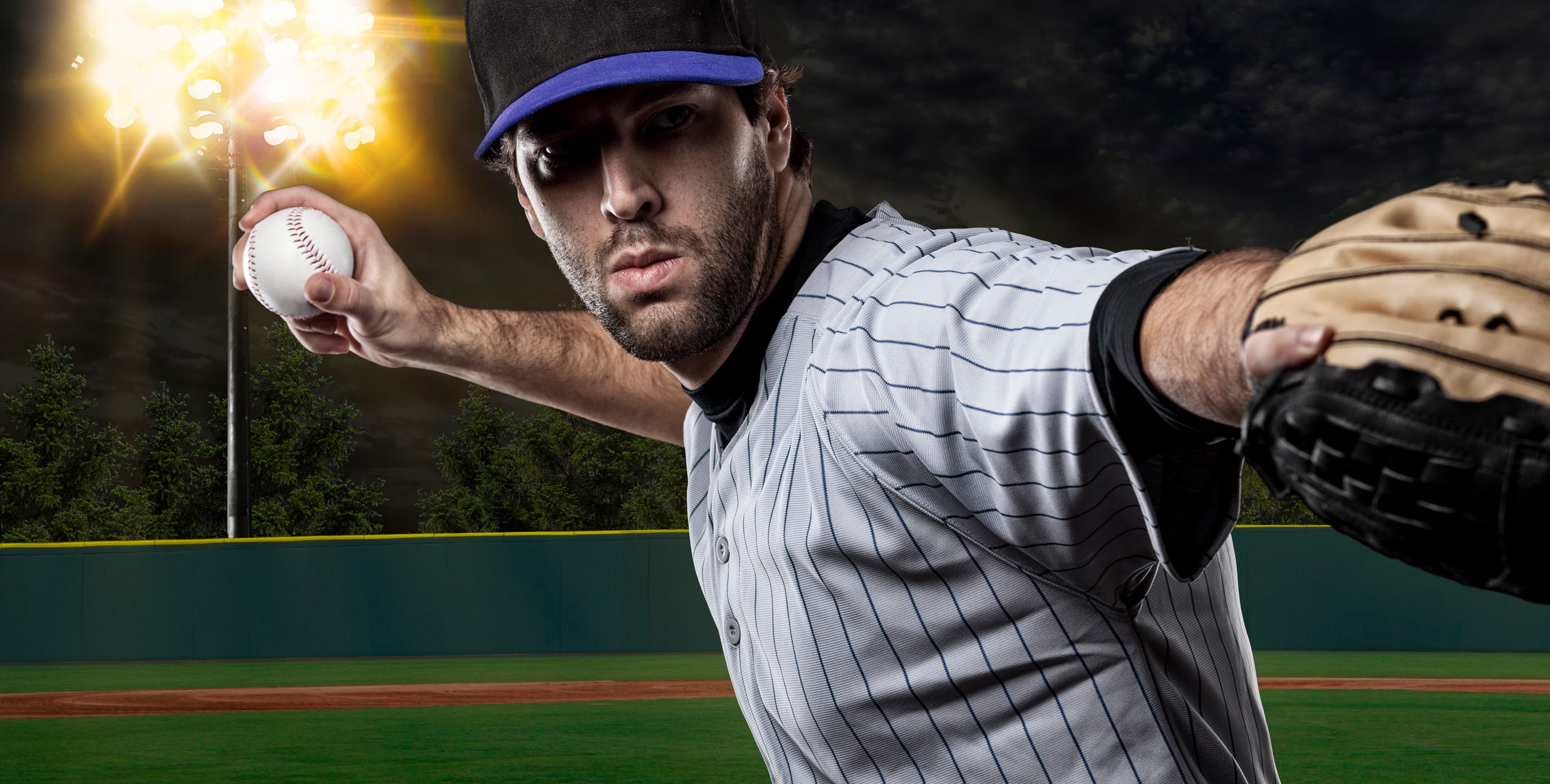 A baseball pitcher prepares to launch his fastball in a brightly lit baseball stadium at night.