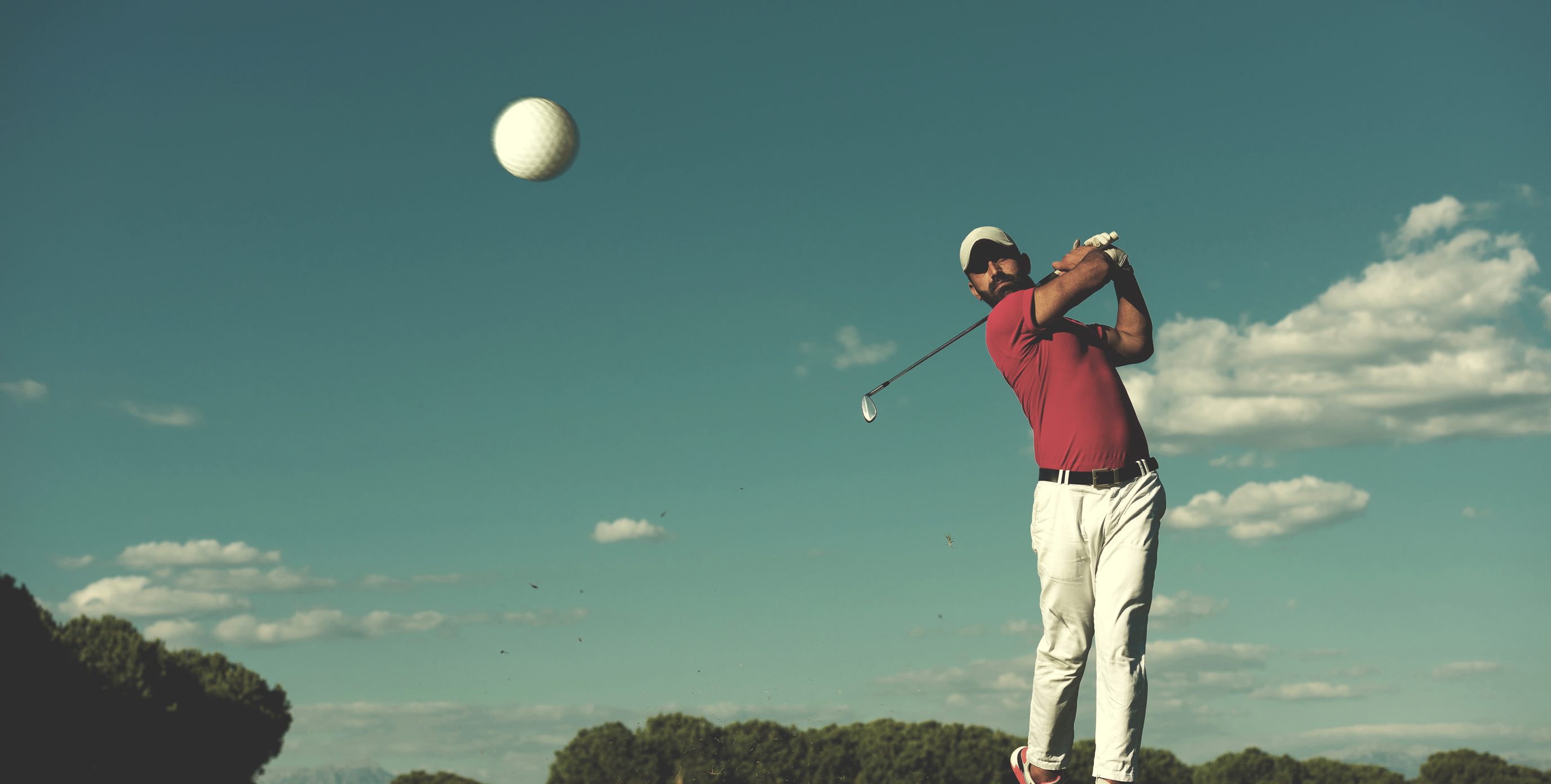 A pro golfer takes a swing at a golf ball on an outside course.