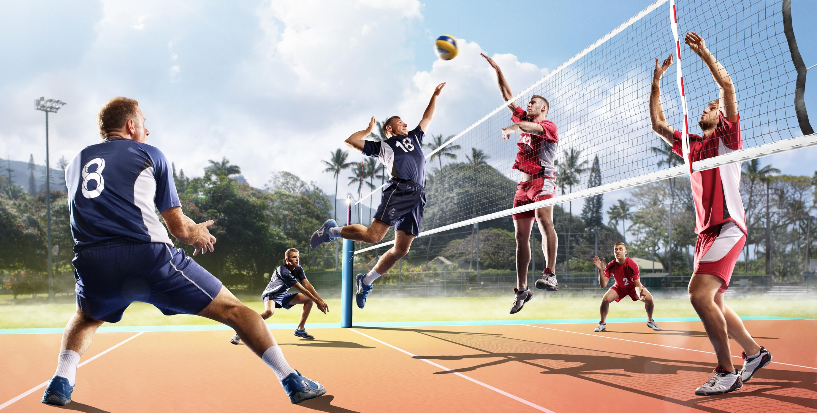 Two mens volleyball teams in a heated match as the blue team prepares a volleyball spike as the red team prepares to counter this volley.