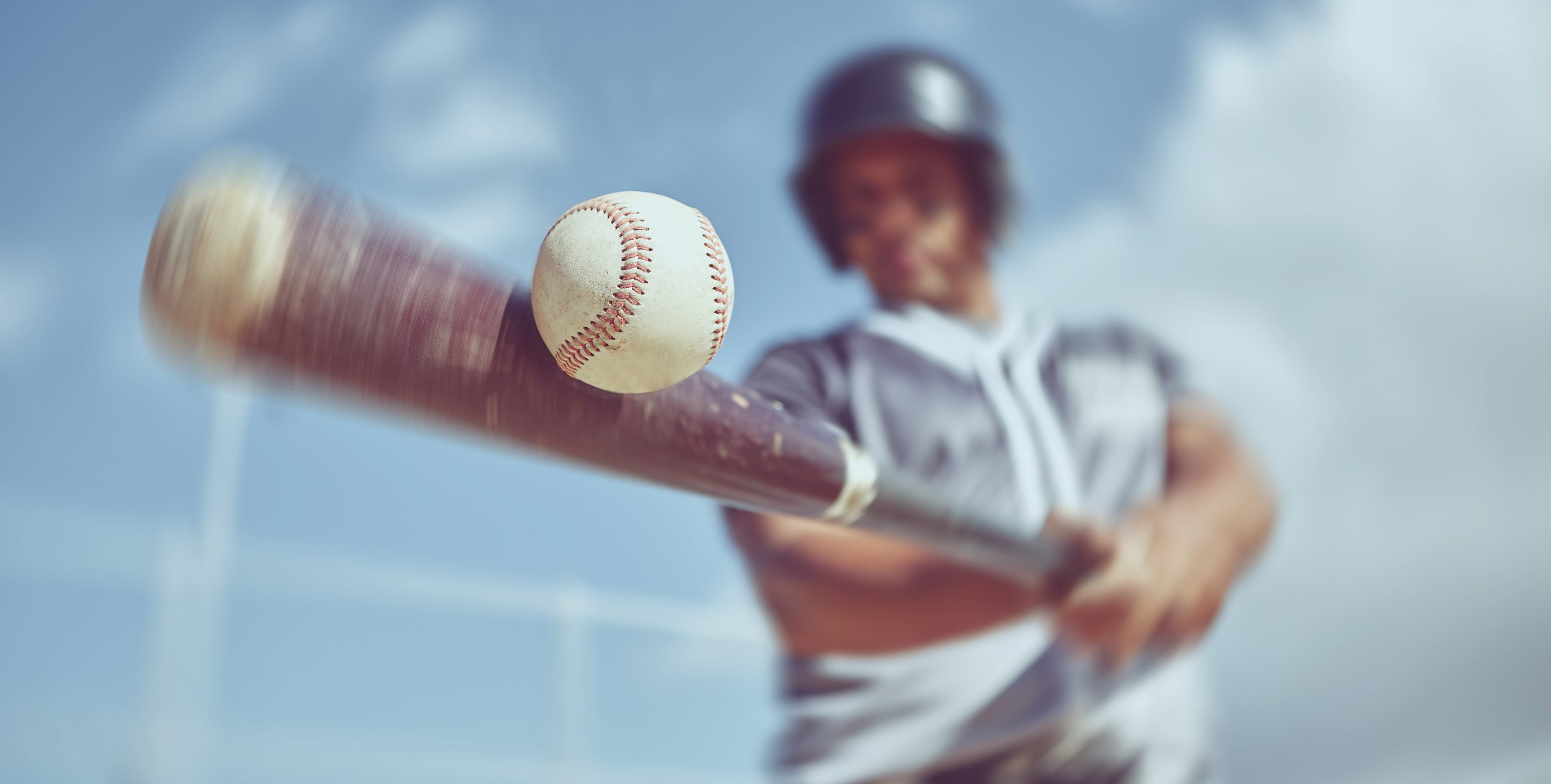 Motion blurred image of a baseball player at bat as he strikes the baseball dead-center with his bat.